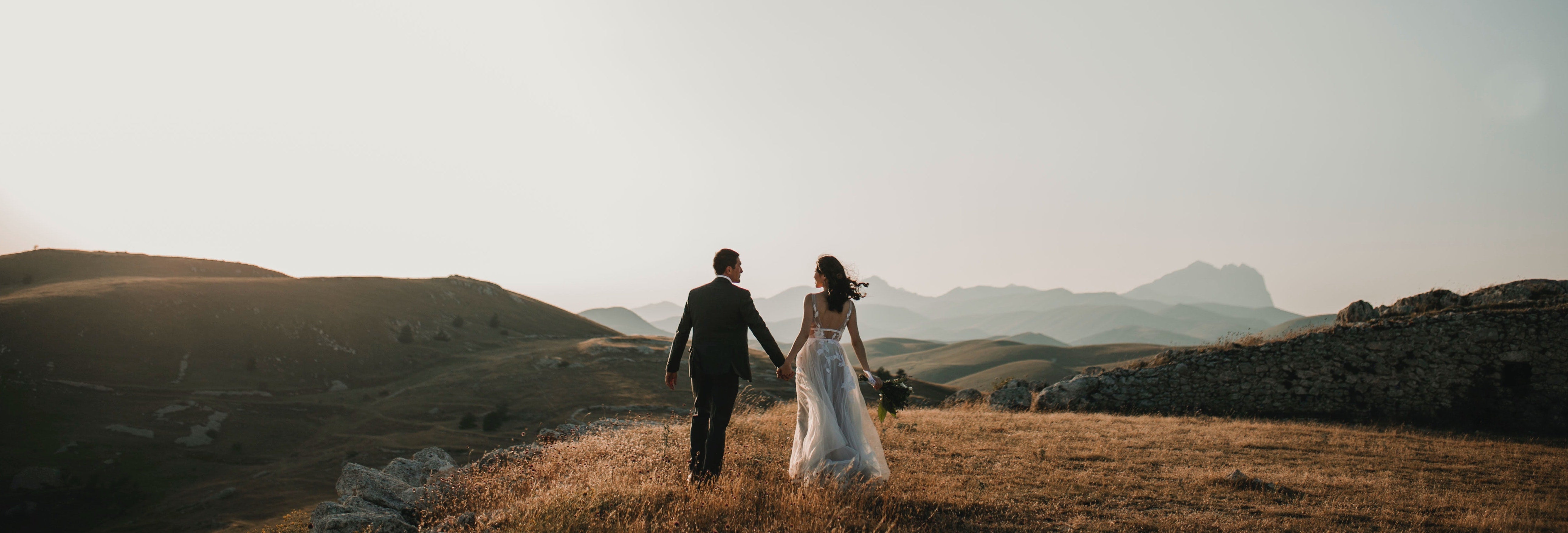 Bride and groom on their wedding day holding hands walking towards the sunset with mountains and hills in the background